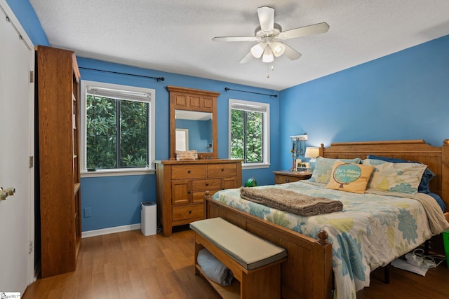 bedroom with light wood-type flooring, baseboards, a textured ceiling, and a ceiling fan