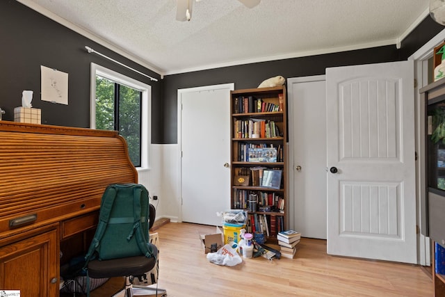 office area featuring a textured ceiling, a wainscoted wall, light wood-style flooring, ceiling fan, and ornamental molding