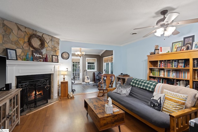 living room featuring ornamental molding, a warm lit fireplace, ceiling fan, wood finished floors, and a chandelier