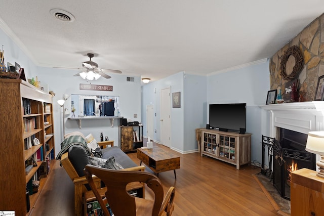 living room with a fireplace with flush hearth, ceiling fan, crown molding, and wood finished floors