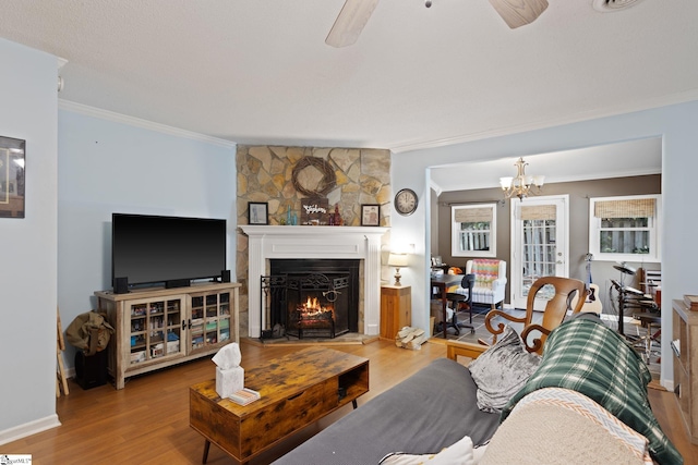 living room featuring crown molding, a stone fireplace, wood finished floors, a ceiling fan, and a chandelier