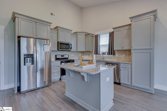 kitchen with appliances with stainless steel finishes, gray cabinets, a kitchen island, a towering ceiling, and tasteful backsplash