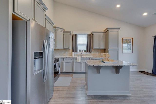 kitchen featuring appliances with stainless steel finishes, gray cabinets, a kitchen bar, backsplash, and lofted ceiling