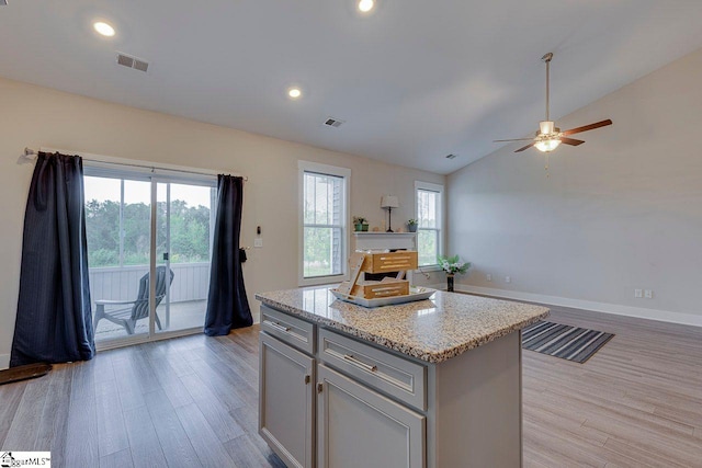 kitchen featuring light wood finished floors, a ceiling fan, lofted ceiling, a center island, and light stone countertops