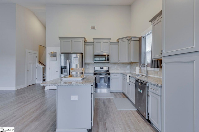 kitchen featuring appliances with stainless steel finishes, a towering ceiling, a sink, backsplash, and gray cabinetry