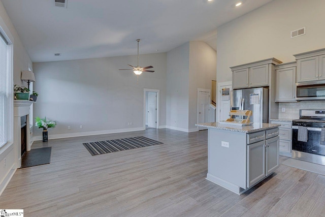 kitchen with stainless steel appliances, gray cabinetry, open floor plan, backsplash, and high vaulted ceiling