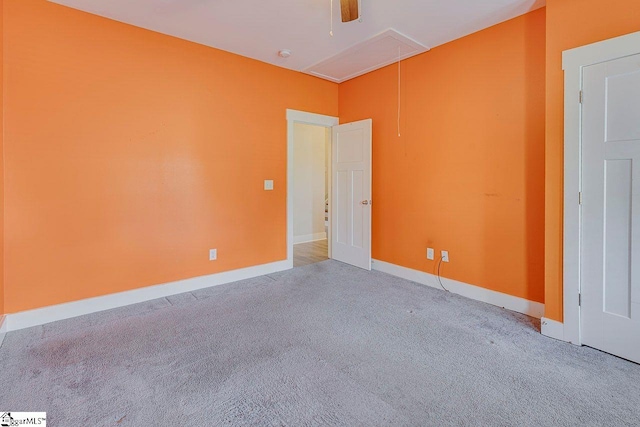 carpeted empty room featuring attic access and baseboards
