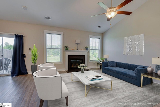 living area with wood finished floors, a glass covered fireplace, ceiling fan, baseboards, and high vaulted ceiling
