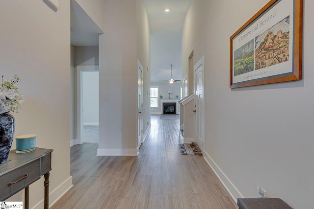 corridor featuring light wood-type flooring, a high ceiling, and baseboards