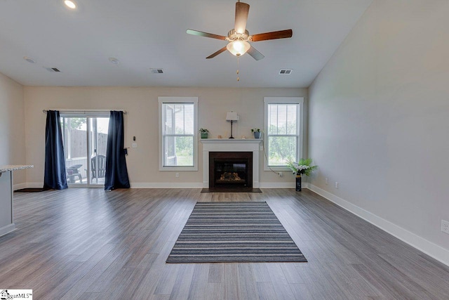unfurnished living room featuring healthy amount of natural light, wood finished floors, ceiling fan, and a fireplace with flush hearth