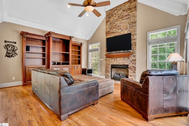 living room with crown molding, a ceiling fan, light wood-type flooring, a stone fireplace, and baseboards