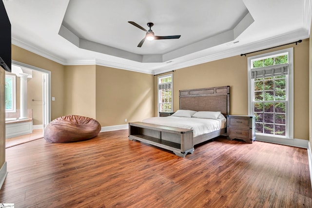 bedroom with a raised ceiling, wood finished floors, multiple windows, ornamental molding, and baseboards