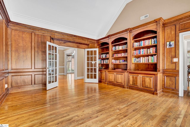 empty room featuring french doors, light wood-style flooring, crown molding, built in shelves, and high vaulted ceiling
