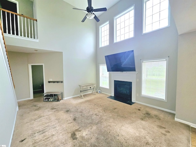 living area featuring a towering ceiling, baseboards, carpet floors, a fireplace with flush hearth, and ceiling fan