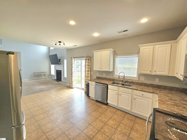 kitchen featuring stainless steel appliances, a sink, open floor plan, white cabinetry, and a fireplace