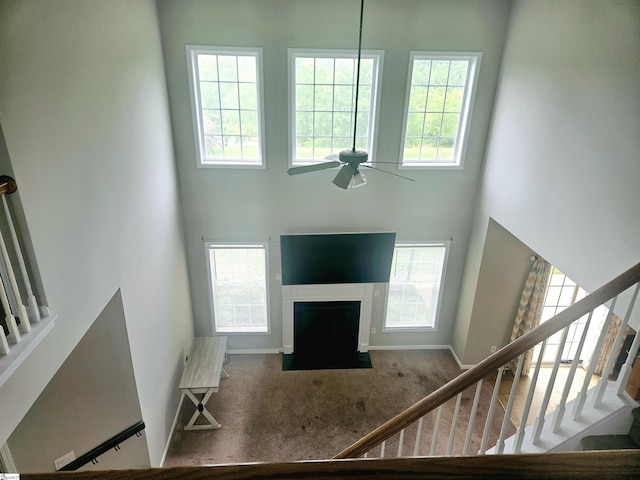 carpeted entryway featuring a high ceiling, stairway, ceiling fan, plenty of natural light, and baseboards