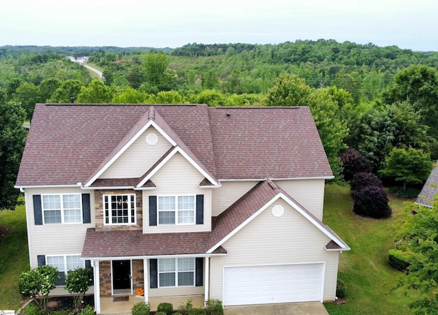 view of front of home featuring a wooded view, roof with shingles, concrete driveway, and a garage