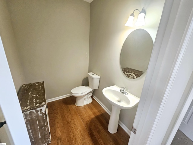 half bathroom with baseboards, wood finished floors, and toilet