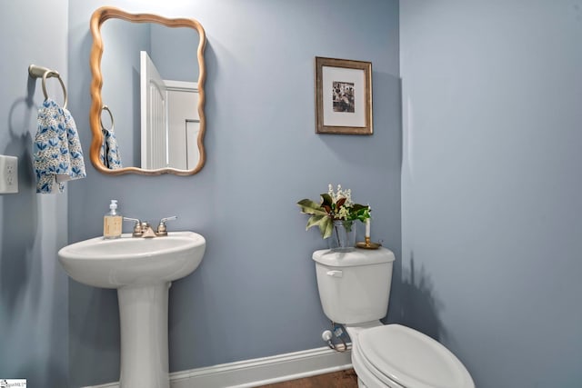 half bath featuring toilet, baseboards, wood finished floors, and a sink