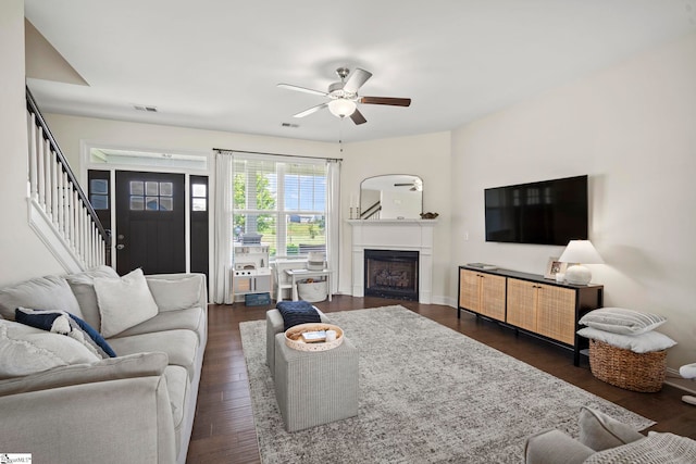 living room featuring stairway, a ceiling fan, dark wood-style flooring, and a fireplace
