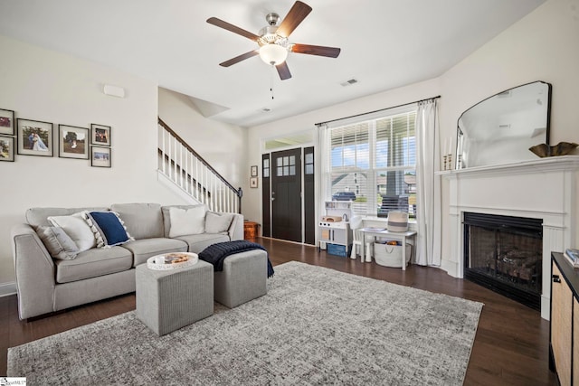 living area with stairway, a ceiling fan, a fireplace, and dark wood-style flooring