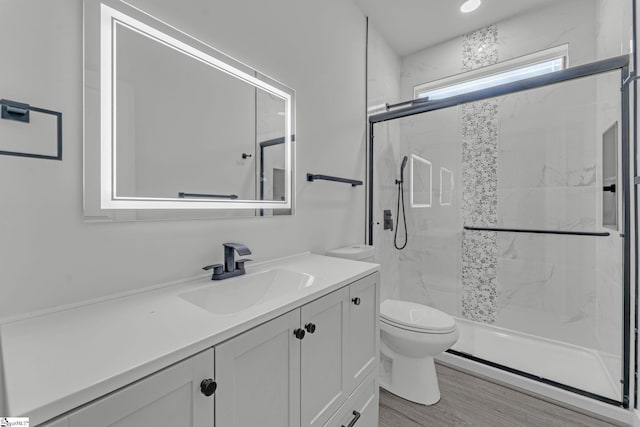 bathroom featuring toilet, a marble finish shower, vanity, and wood finished floors