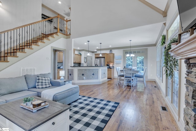 living room with light wood-style floors, stairway, crown molding, a towering ceiling, and a chandelier