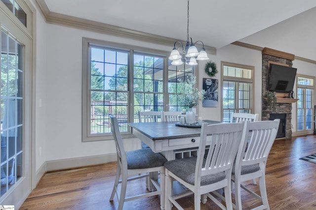 dining area featuring crown molding, plenty of natural light, a stone fireplace, wood finished floors, and baseboards