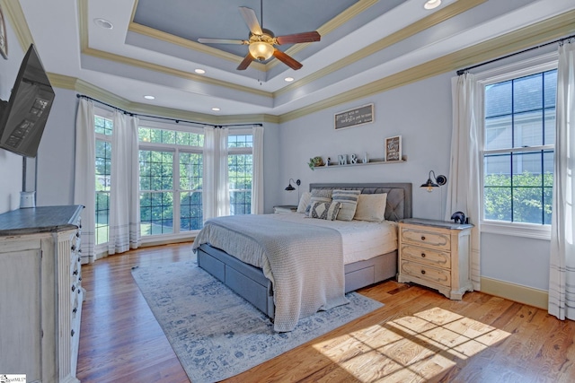 bedroom featuring multiple windows, ornamental molding, a tray ceiling, light wood-style flooring, and baseboards