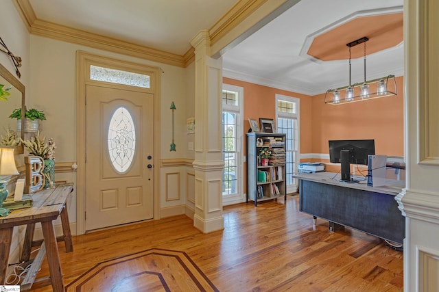 foyer entrance with ornate columns, light wood-style floors, and ornamental molding