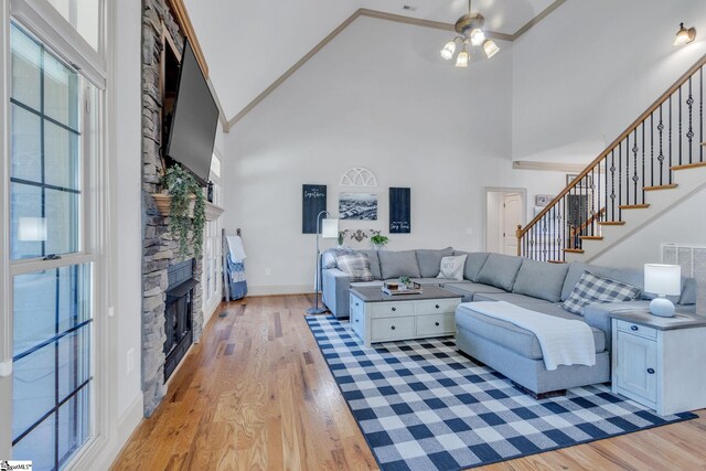 living room with high vaulted ceiling, a stone fireplace, ceiling fan, light wood-style flooring, and stairs