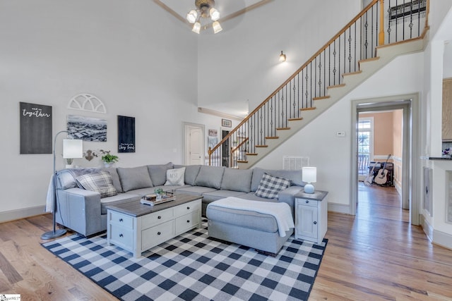 living area with a high ceiling, light wood-style flooring, stairway, ceiling fan, and baseboards
