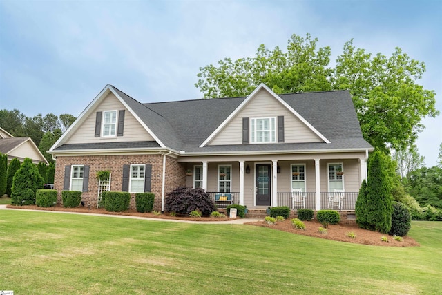 view of front facade featuring a front lawn, a shingled roof, a porch, and brick siding