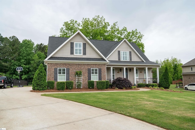 view of front facade with covered porch, a front lawn, brick siding, a shingled roof, and concrete driveway