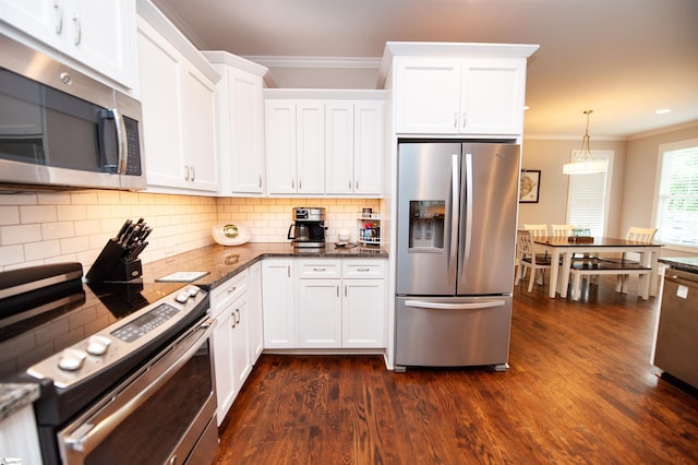 kitchen with appliances with stainless steel finishes, ornamental molding, dark wood-style flooring, white cabinetry, and dark stone counters