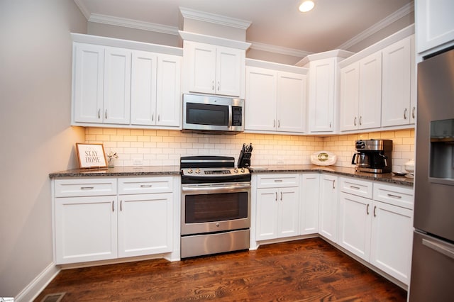 kitchen featuring stainless steel appliances, ornamental molding, dark stone countertops, white cabinets, and backsplash