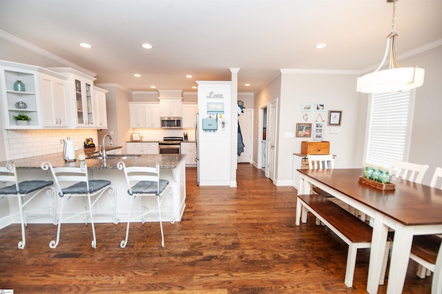 kitchen with appliances with stainless steel finishes, a peninsula, a sink, white cabinets, and dark wood-style flooring