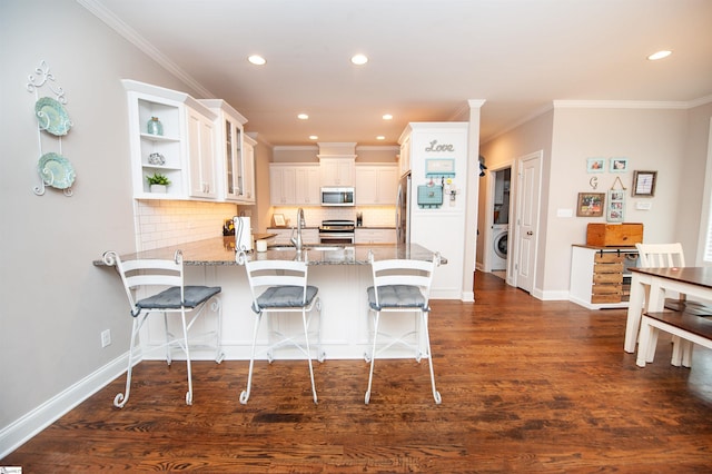 kitchen with washer / dryer, appliances with stainless steel finishes, a peninsula, light stone countertops, and decorative backsplash