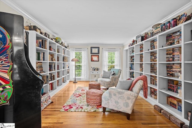 living area featuring bookshelves, ornamental molding, and wood finished floors