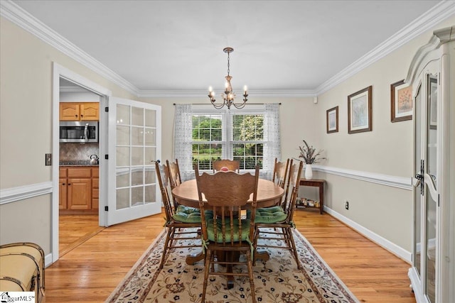 dining space featuring a chandelier, light wood-type flooring, crown molding, and baseboards