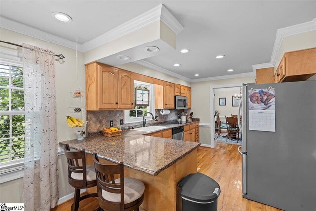 kitchen featuring stainless steel appliances, a peninsula, dark stone countertops, a breakfast bar, and light wood-type flooring