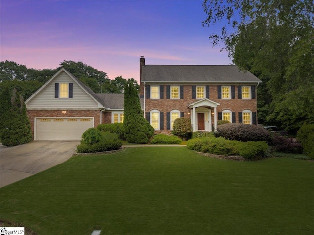 colonial-style house featuring a chimney, driveway, brick siding, a yard, and an attached garage