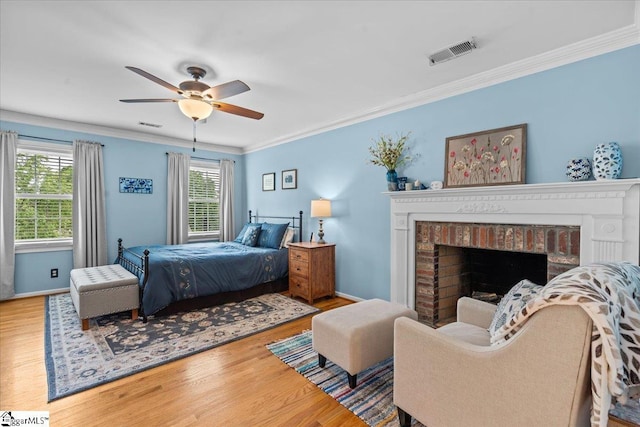 bedroom featuring multiple windows, ornamental molding, wood finished floors, and a brick fireplace