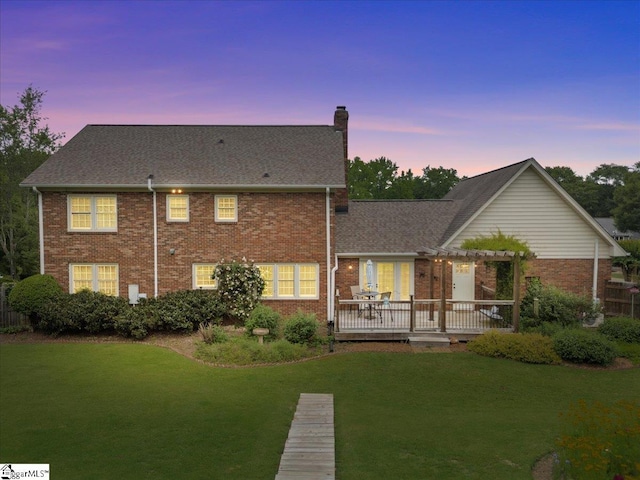rear view of house with a pergola, brick siding, a chimney, a lawn, and a wooden deck