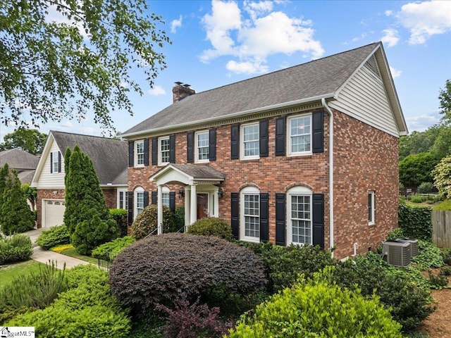 colonial-style house with brick siding, a chimney, fence, and cooling unit