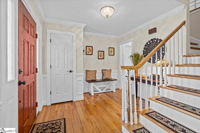 entrance foyer with light wood-type flooring, stairs, crown molding, a wainscoted wall, and a decorative wall