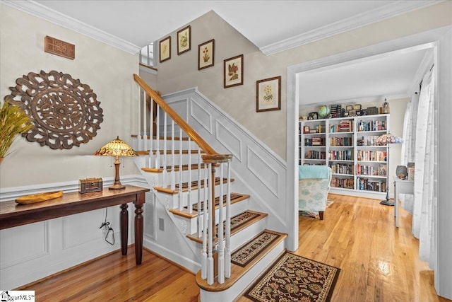 stairway with wood finished floors, ornamental molding, a decorative wall, and a wainscoted wall