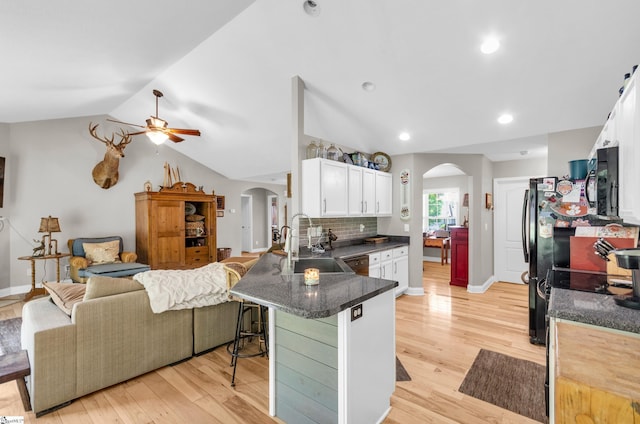 kitchen featuring arched walkways, a sink, a ceiling fan, a peninsula, and light wood finished floors