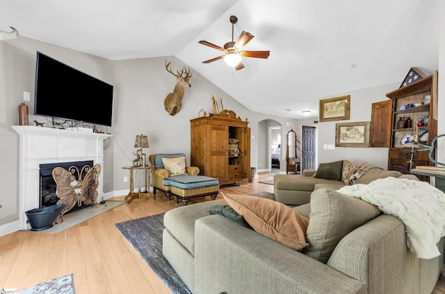 living area with arched walkways, a ceiling fan, wood-type flooring, lofted ceiling, and a fireplace with flush hearth