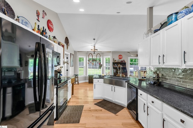 kitchen with black appliances, a sink, a peninsula, lofted ceiling, and white cabinetry